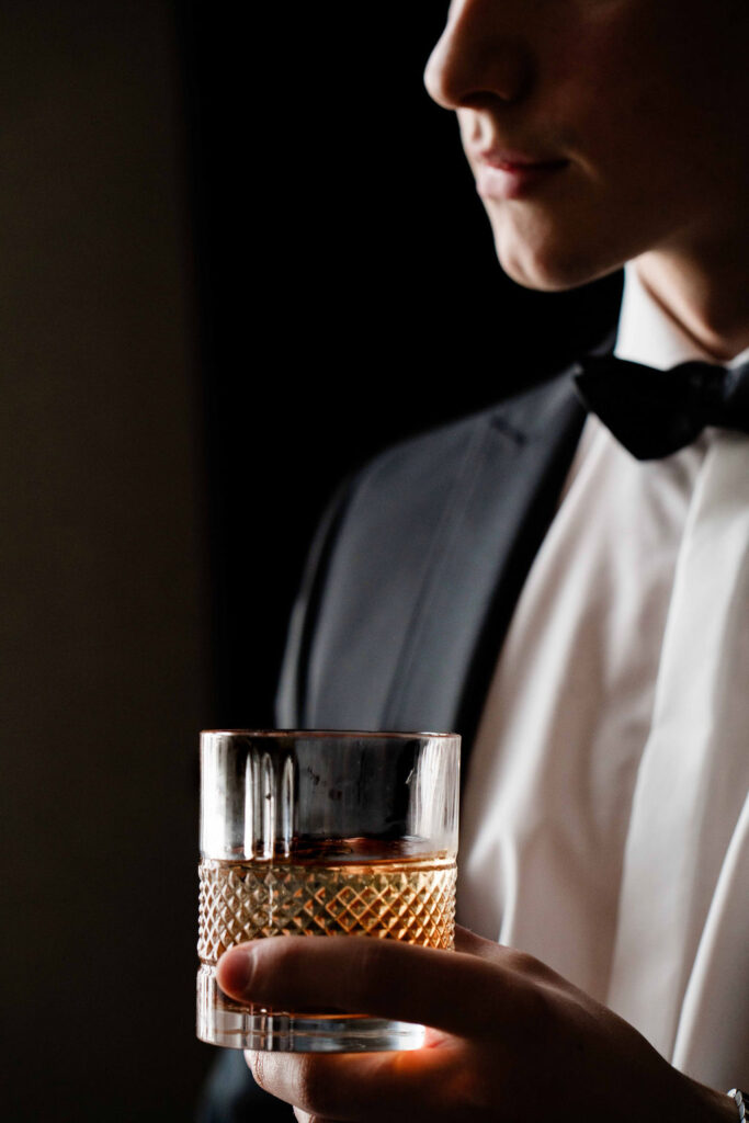 Foto von einem Bräutigam, der im Black Tie Stil gekleidet ist und ein Glas in der Hand trägt