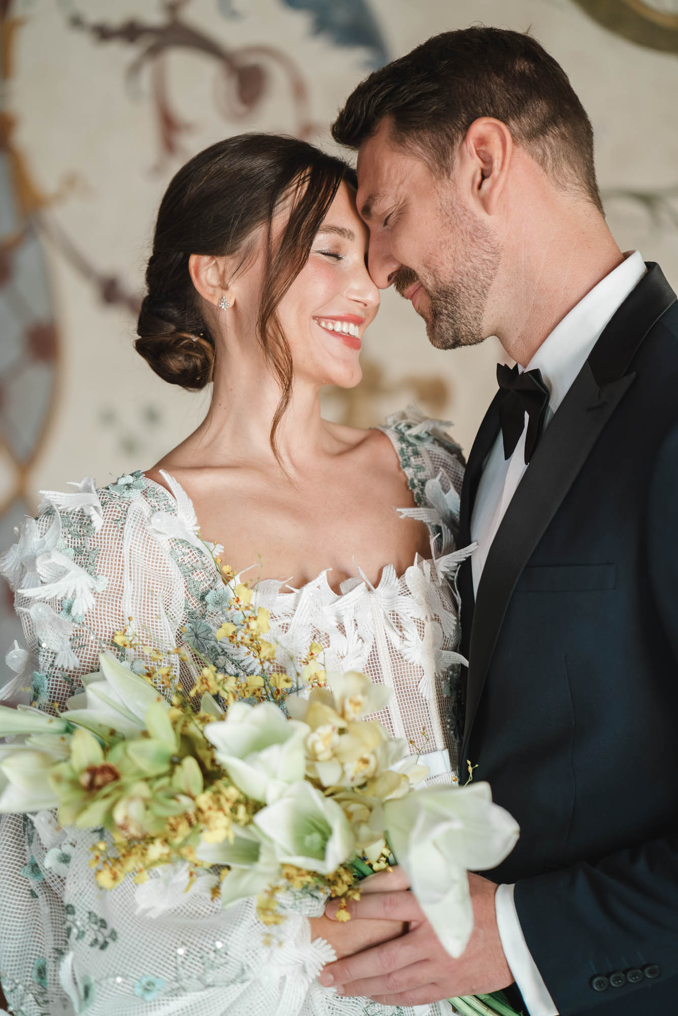 Brautpaar bei einer Hochzeit im Belvedere Wien, Stirn an Stirn vor der Freskenwand, Brautstrauß aus grünen Orchideen und Mimosen