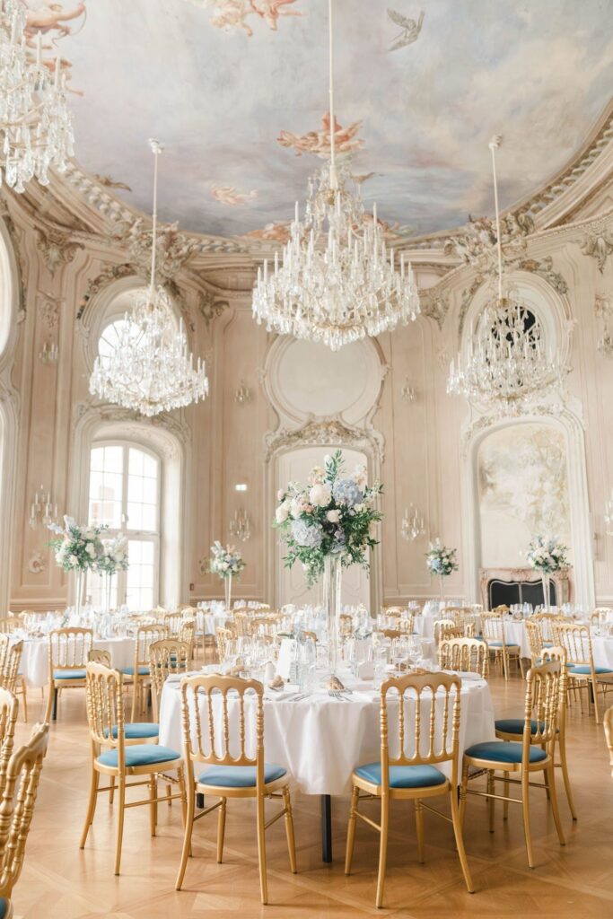 Festsaal in Schloss Laxenburg mit Deckenfresko, Kristalllustern und gedeckten Rundtafeln